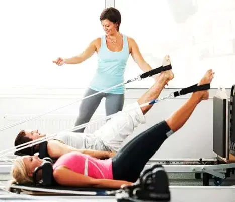 Klinik pilates eğitmeni eşliğinde reformer pilates yapan iki kişi