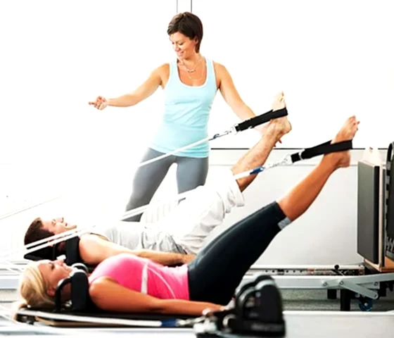 Klinik pilates eğitmeni eşliğinde reformer pilates yapan iki kişi